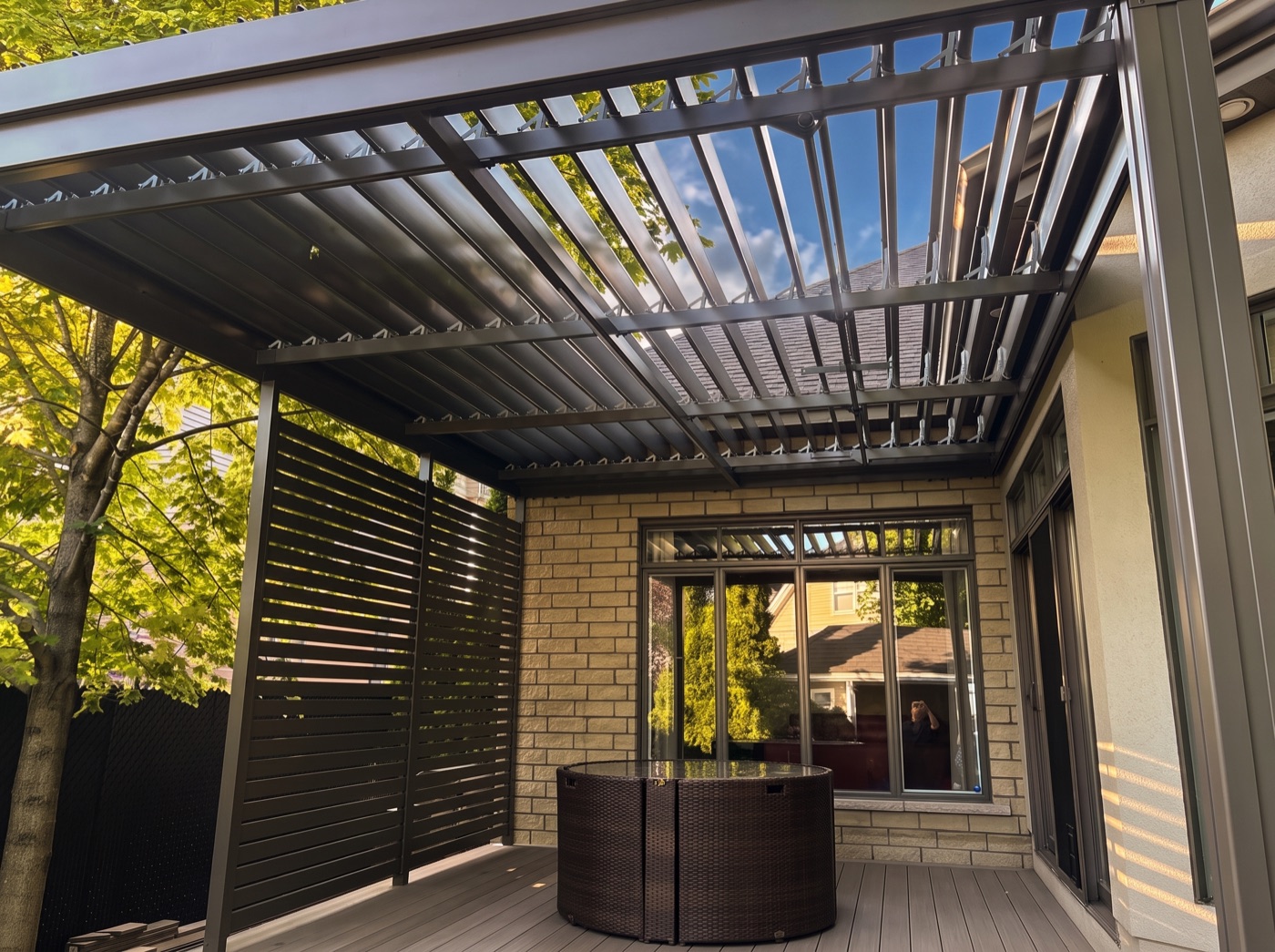 Vue sous une pergola à lames orientables SunLouvre Pergolas, le mur d&rsquo;intimité ferme le côté gauche de la terrasse