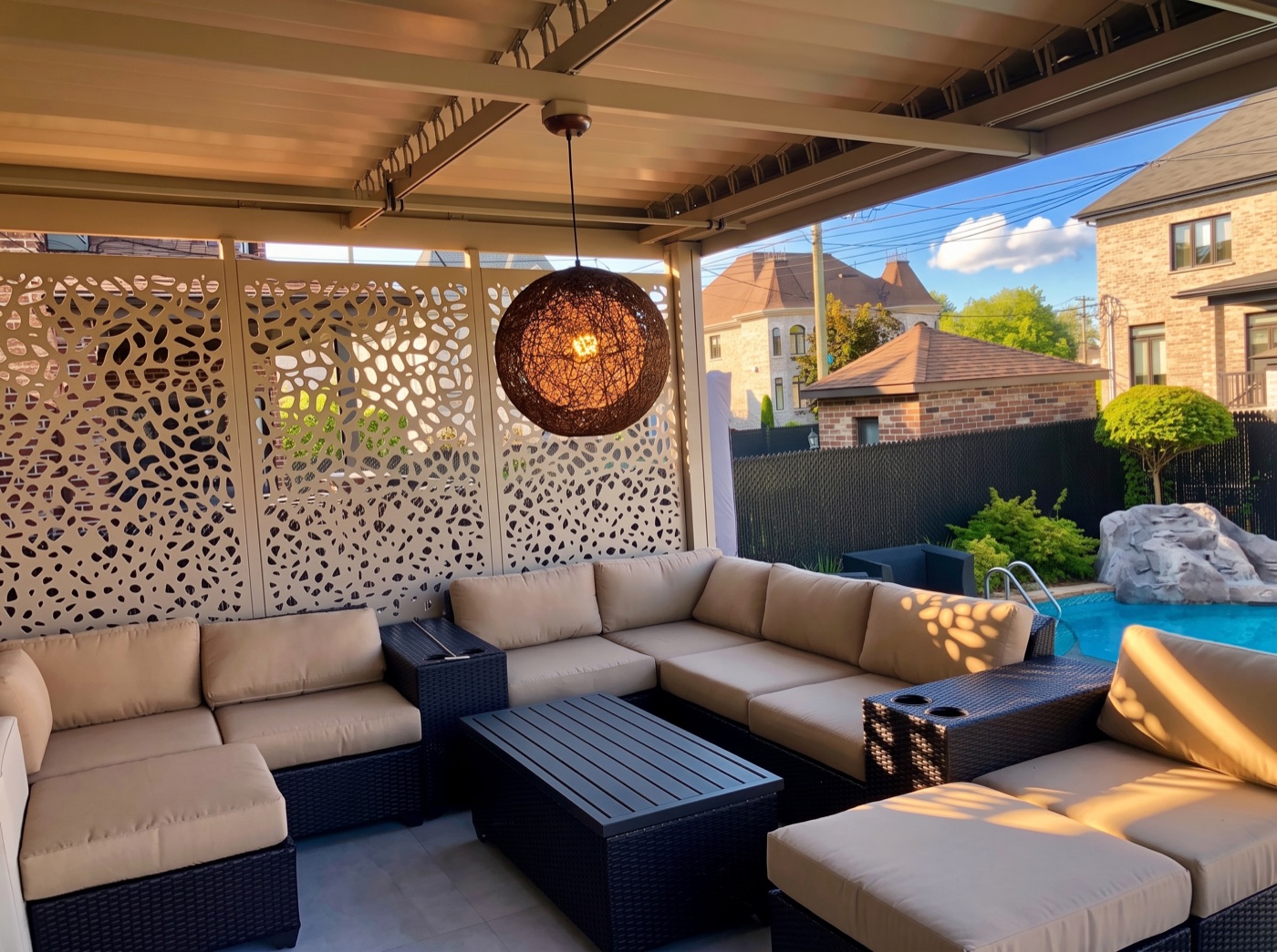Panneaux d&rsquo;intimité crème sous une pergola SunLouvre Pergolas, le motif découpé projette son dessin sur le mobilier de salon