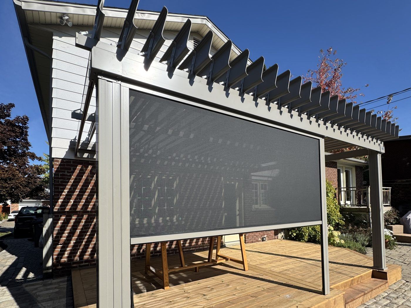Toile motorisée partiellement déployée sous une pergola SunLouvre Pergolas à lames orientables, laissant voir la maison et le jardin au travers du tissu
