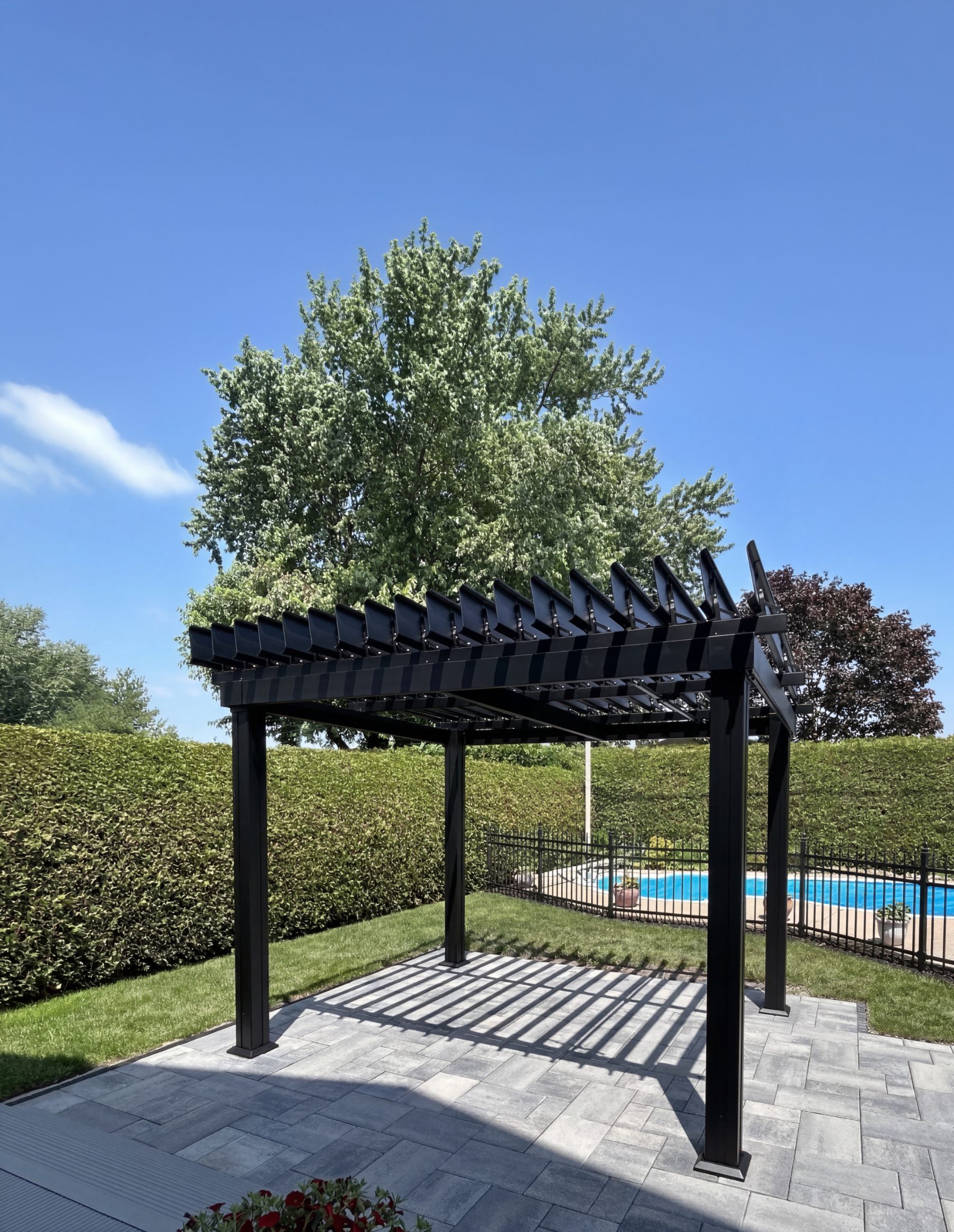 SunLouvre Classic Model 10x12 in black, installed by a pool, shade controlled by tilting louvers