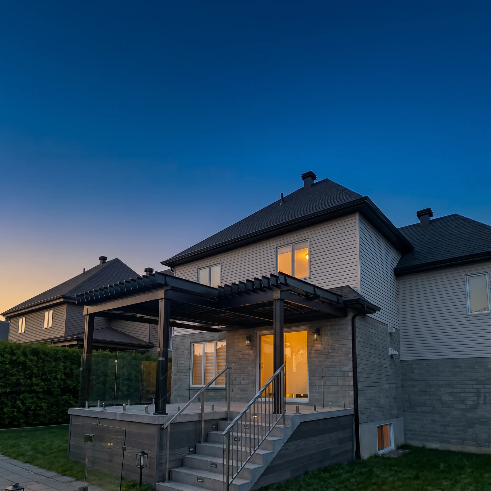 Pergola noire adossée à une maison, au-dessus d'une terrasse, au crépuscule