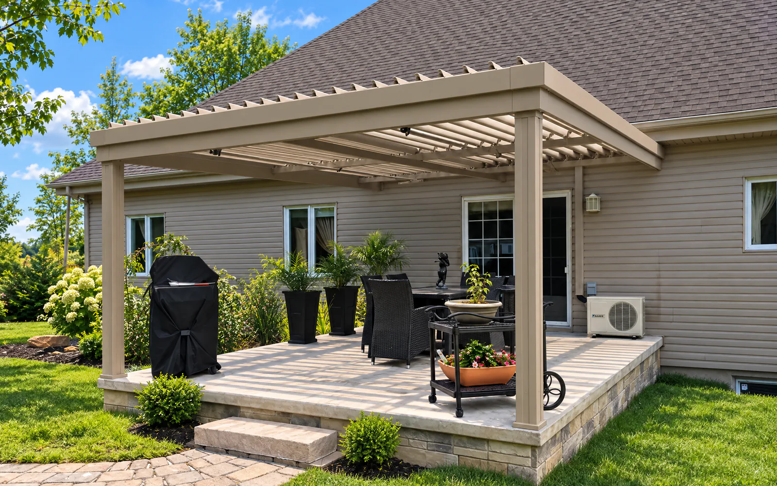 Pergola à lames intégrées SunLouvre Pergolas couleur sable au-dessus d'une terrasse surélevée, derrière une maison