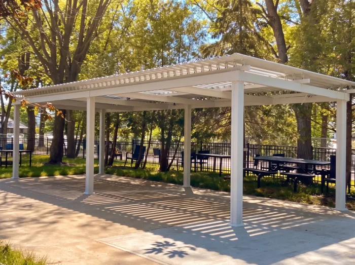 White pergola over a paved area among the trees, Résidence Angelica in Montréal-Nord