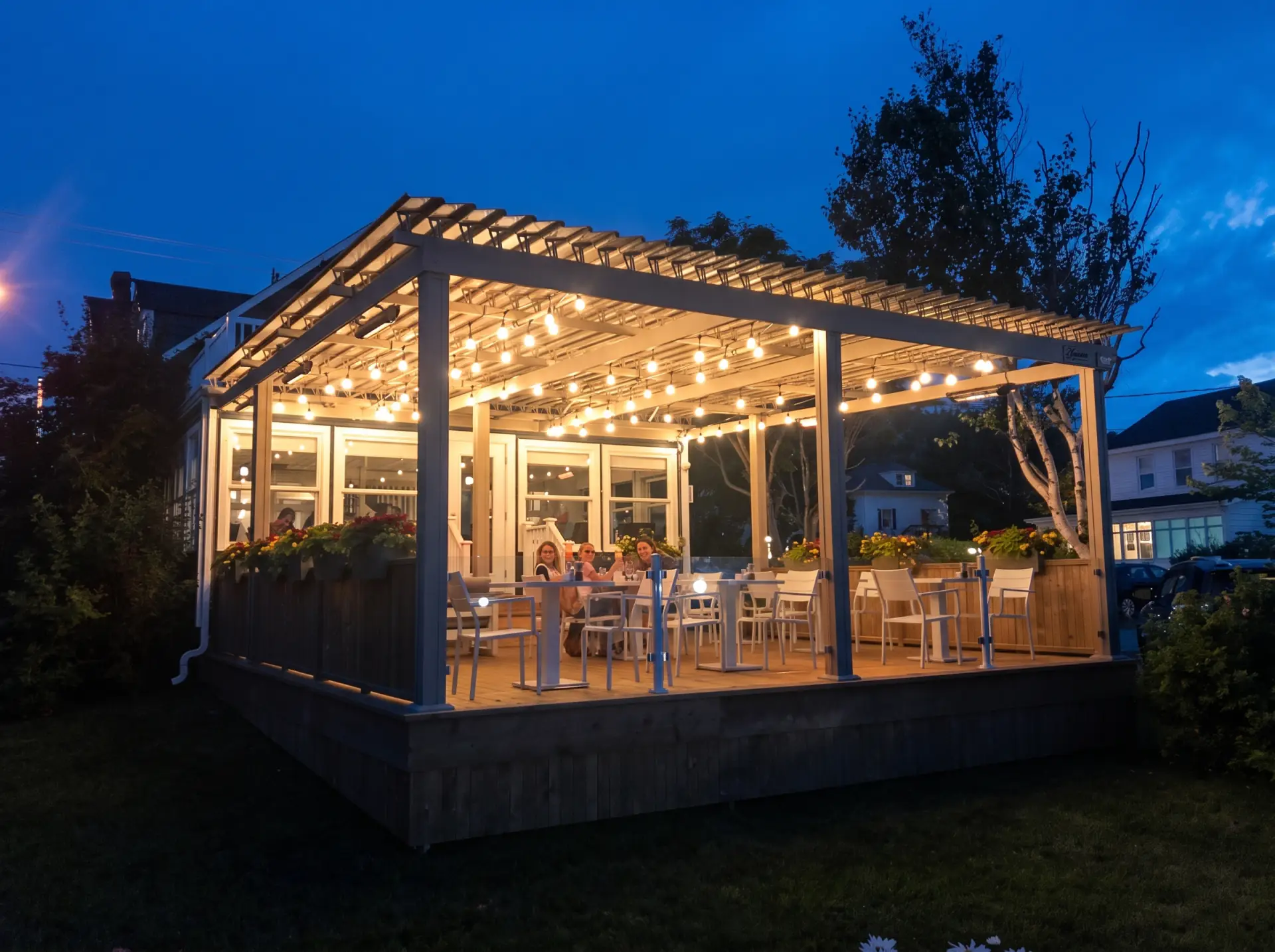 Terrasse illuminée le soir sous la pergola et ses guirlandes, Auberge Les 3 Soeurs à Percé