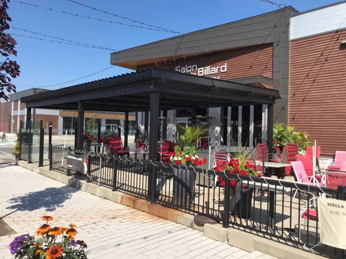 Black pergola over the flower-lined terrace with red chairs, Salon du Billard in Mégantic