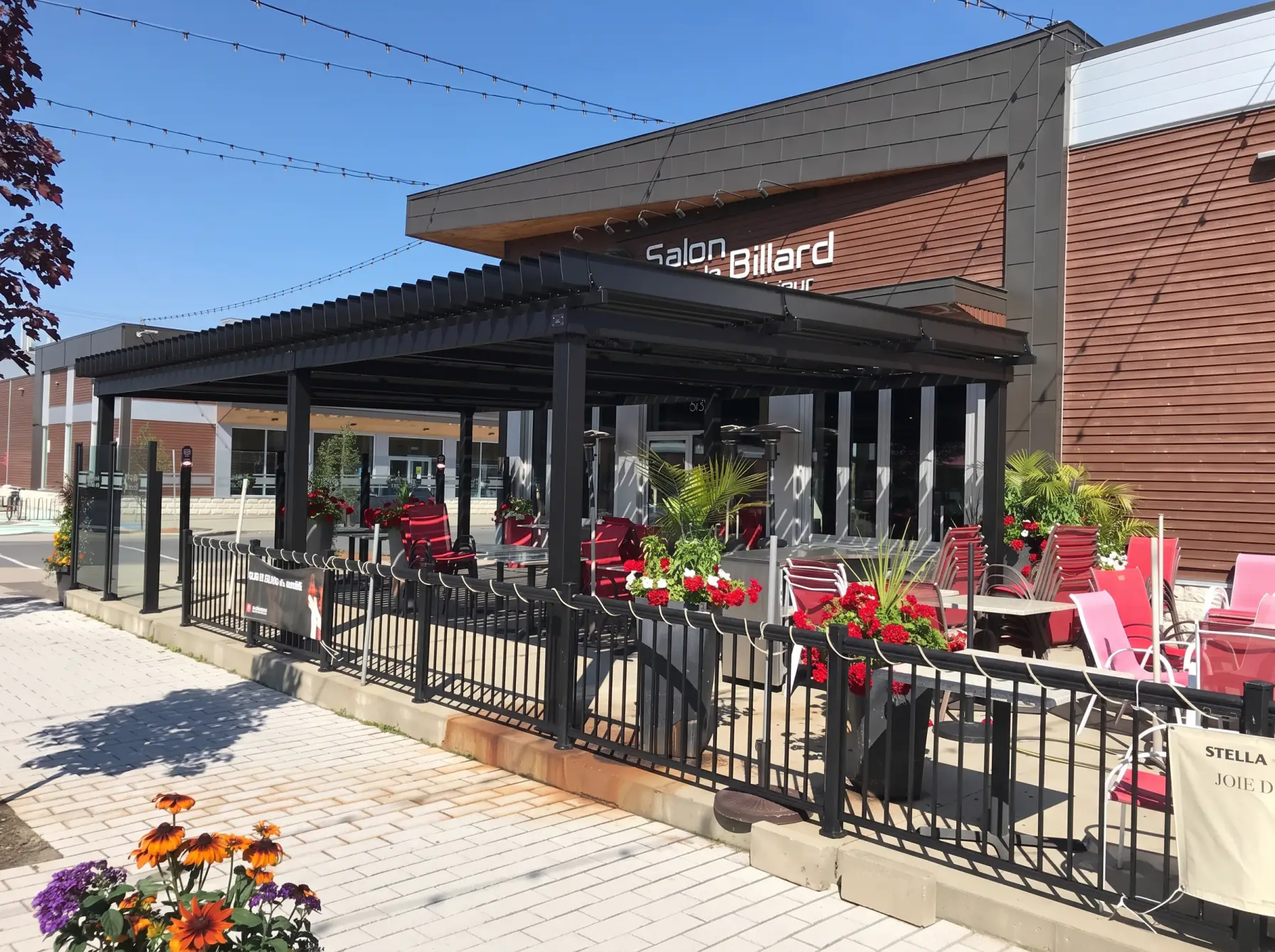 Black pergola over the flower-lined terrace with red chairs, Salon du Billard in Mégantic