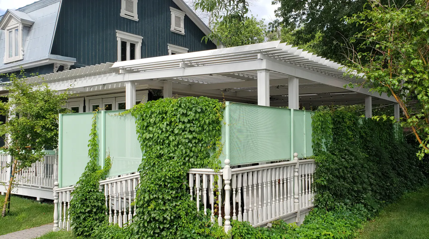 Pergola blanche adossée au bâtiment vert, clôture couverte de lierre, Le Boating Club à Laval