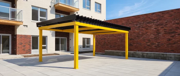 Pergola jaune au-dessus de la cour pavée de l'immeuble de brique, Le Carré Radisson à Trois-Rivières