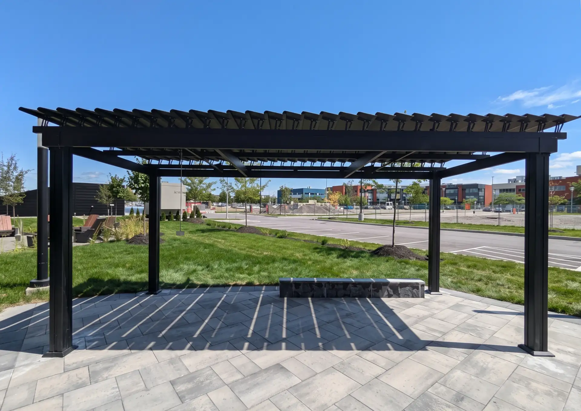 Black pergola over the paved plaza edged with lawn, Centropolis in Laval