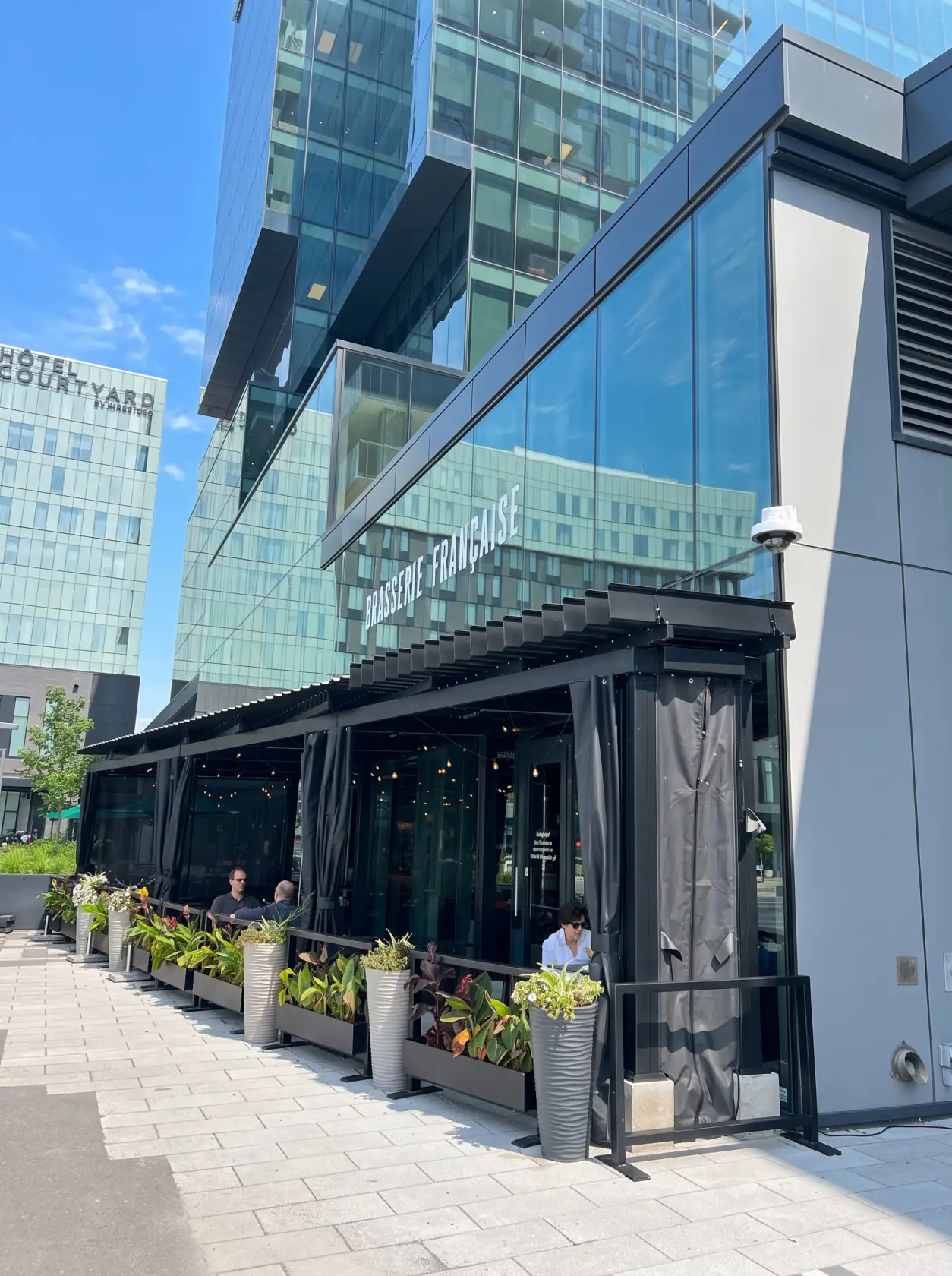 Glazed terrace and dark pergola at the foot of the glass tower, Chez Lionel in Brossard