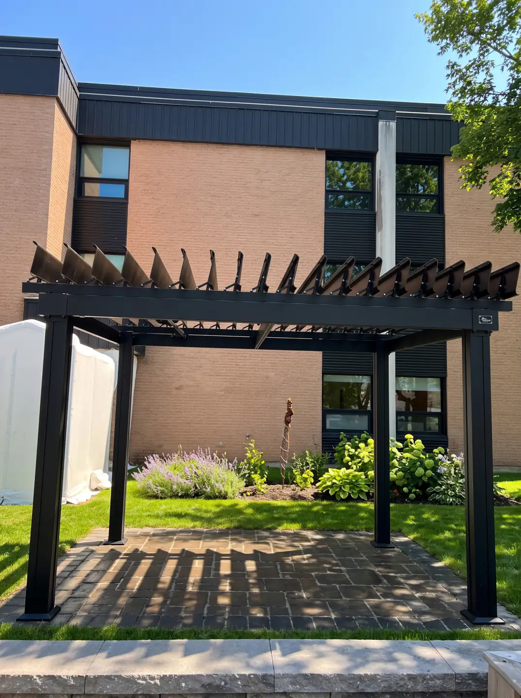 Black pergola over the paved walkway alongside the brick building, CHSLD de Loretteville in Québec