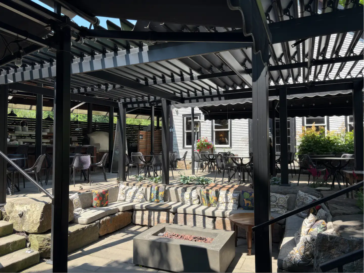 Pergola noire au-dessus de la terrasse de pierre et sa longue banquette, Domaine Jolivent à Lac-Brome