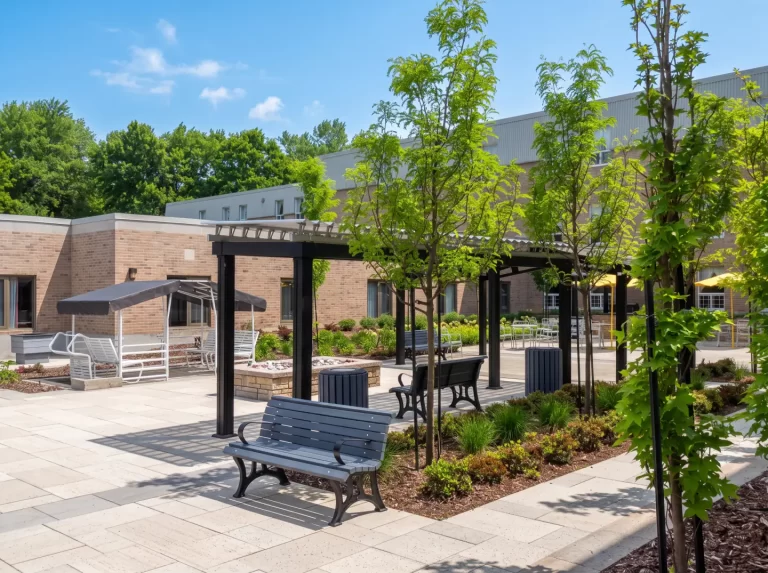 Bancs et jeunes arbres sous les pergolas noires de la cour, Centre d'hébergement Hubert-Maisonneuve à Rosemère