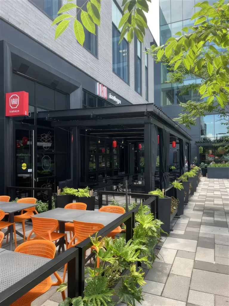 Terrasse aux chaises orange sous la pergola noire, Iru Izakaya à Brossard
