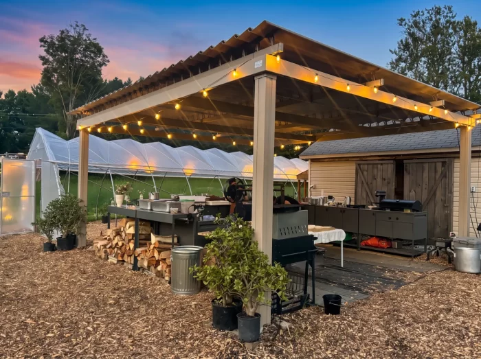 Outdoor kitchen under a wooden pergola and its string lights, Les Jardins Bolton in Bolton-Est