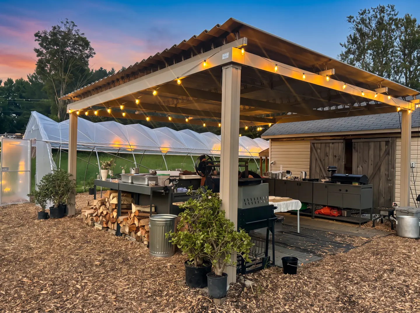 Outdoor kitchen under a wooden pergola and its string lights, Les Jardins Bolton in Bolton-Est
