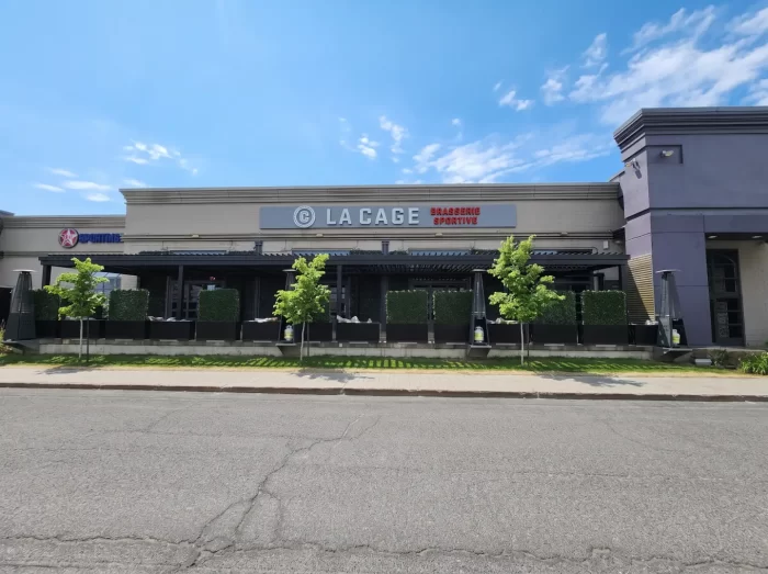 Black pergola along the façade seen from across the street, La Cage in Boucherville