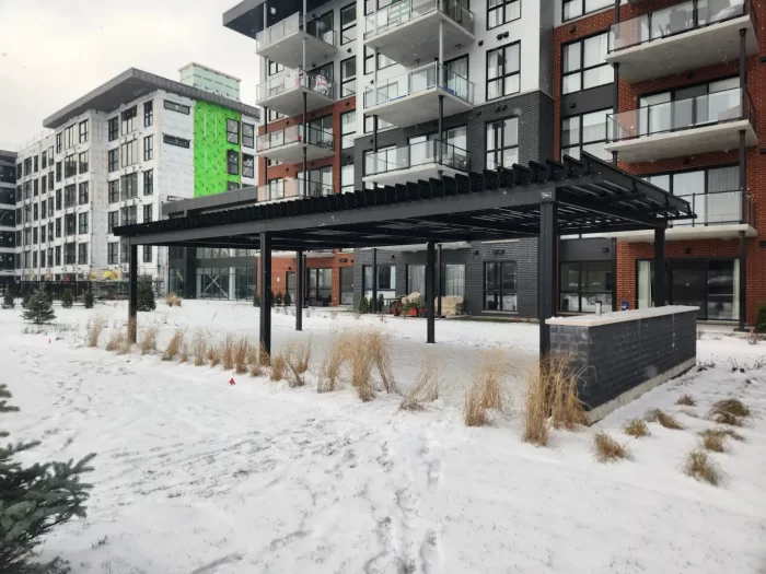 Pergola noire le long de l'immeuble de condos sous la neige, Projet Citiluxx à Saint-Hubert