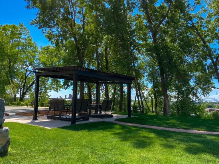 Pergola sombre au-dessus d'une terrasse pavée entre les arbres, Résidence Place Belvédère à Trois-Rivières