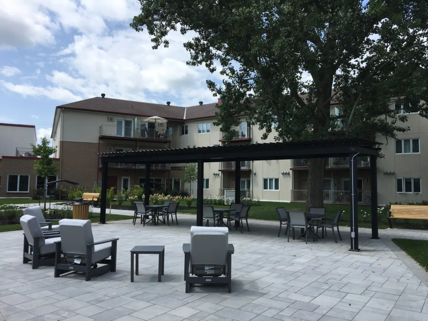 Cour pavée et fauteuils de jardin sous une pergola noire, Résidences Les Richeloises à McMasterville