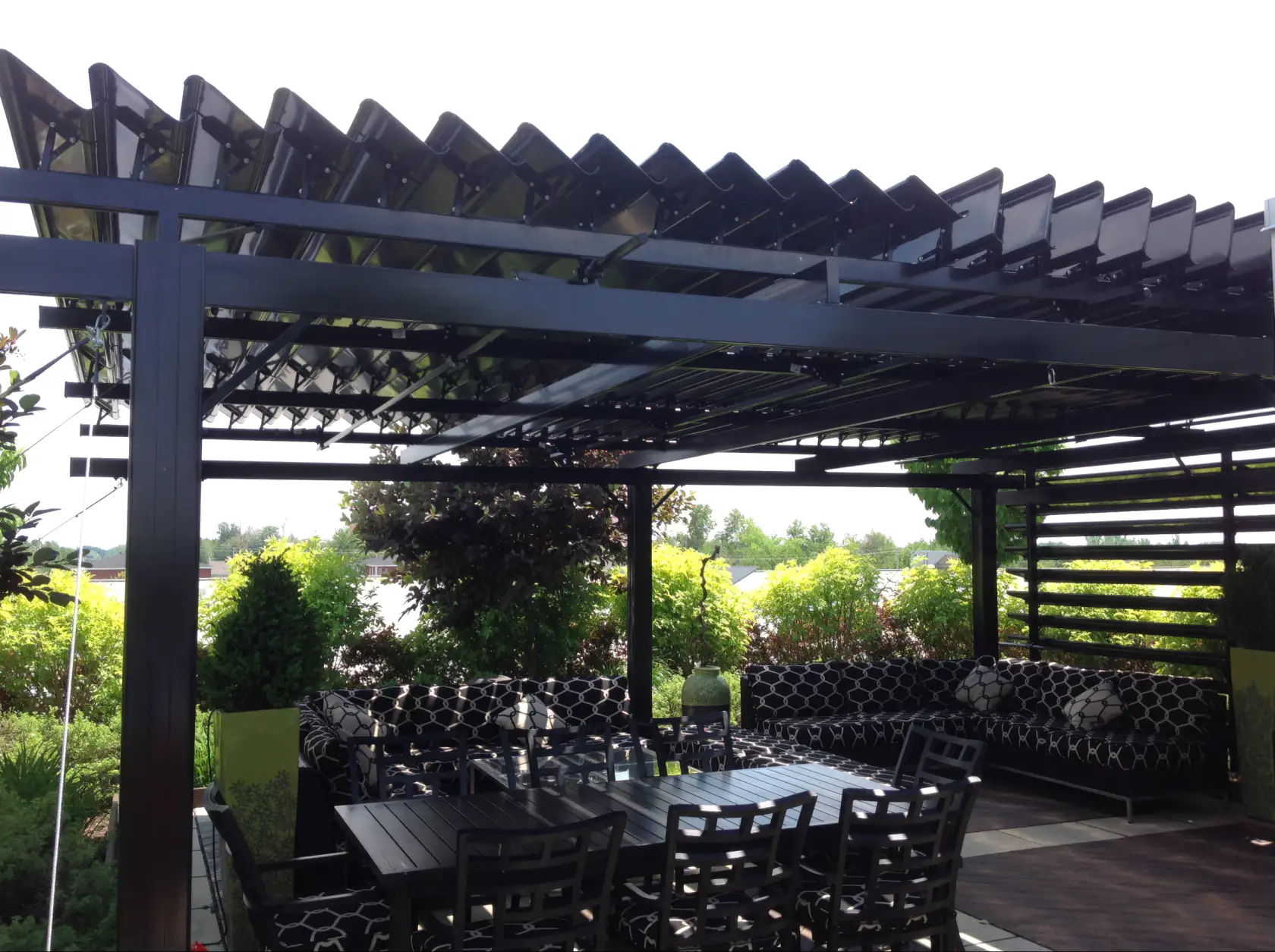 Outdoor lounge and dining table under a black louvered pergola, Soprema Canada in Drummondville