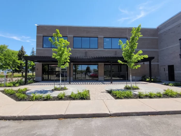 Black pergola over the stone building's entrance walkway, Stelpro Design in Saint-Bruno-de-Montarville
