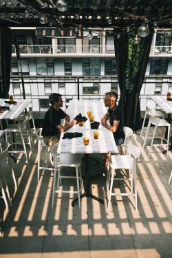 Convives attablés sur la terrasse entre verdure et gratte-ciel, Terrasse Alizé de l'hôtel Humaniti à Montréal